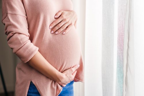 pregnant woman, hands on belly, near window