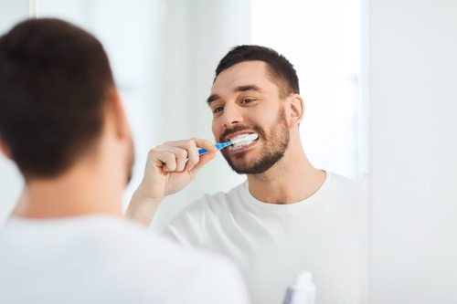 smiling young man brushing teeth and looking at mirror