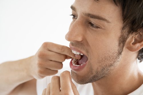 Man flossing his teeth with a white background.