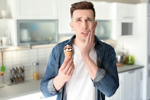 Young man holding his mouth in pain with cold ice cream in a kitchen.